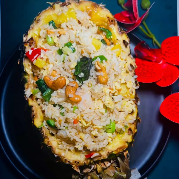 Pineapple fried rice with cashews, vegetables, and shrimp, served in a pineapple half on a black plate.
