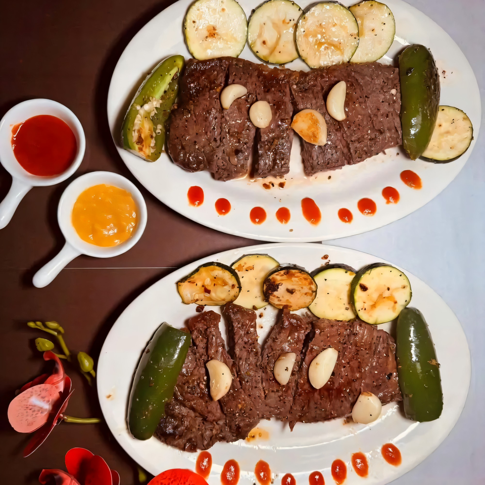 Two plates of sliced steak with roasted zucchini, jalapeños, garlic cloves, and dipping sauces.