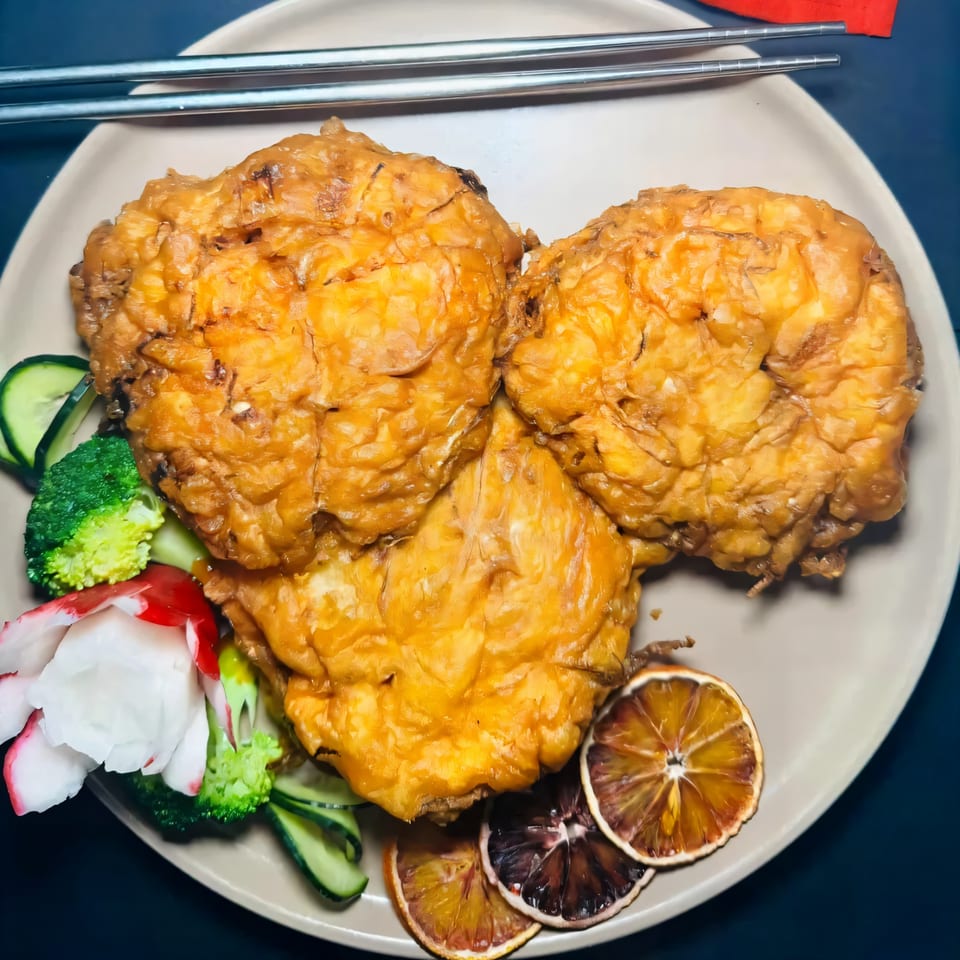 Three golden-brown fried chicken pieces with broccoli, cucumber, radish, and dried orange slices on a plate.