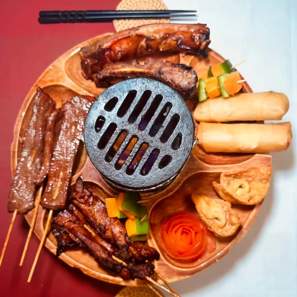 A wooden platter with House of Chou's Chinese appetizers, including ribs, skewers, spring rolls, and fried wontons.