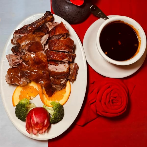 Peking duck, sliced and served with orange, broccoli, and a side of dark sauce.